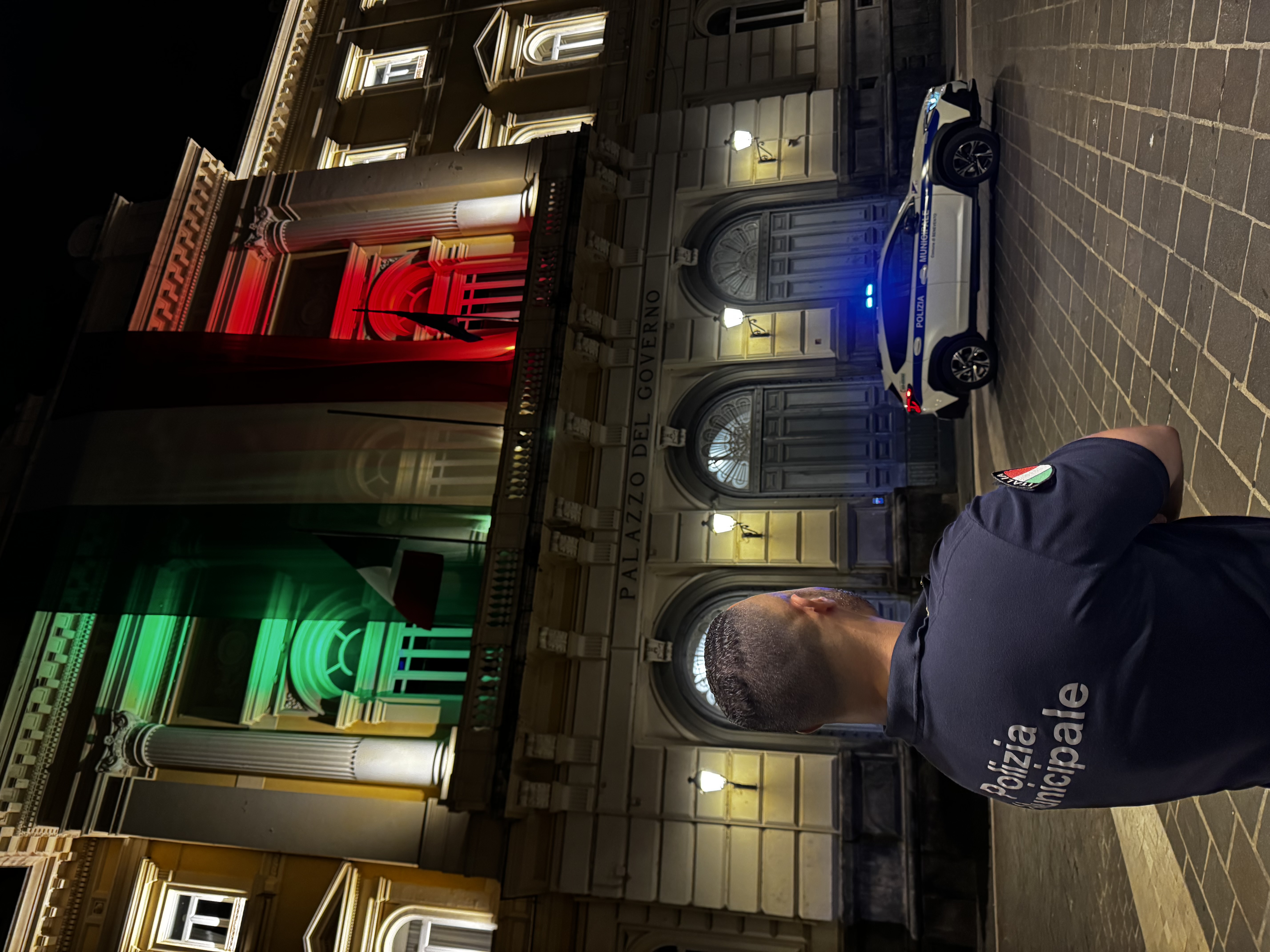 Polizia Municipale davanti alla Prefettura, in una suggestiva atmosfera serale, con la bandiera nazionale esposta in occasione della festa.